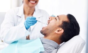 Dentist in white coat and blue gloves examining man's mouth